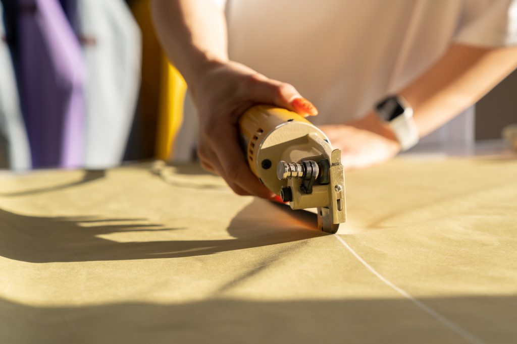 Designer use electric cutter for cutting fabric work in studio. Closeup of tailor cut cloth to sew